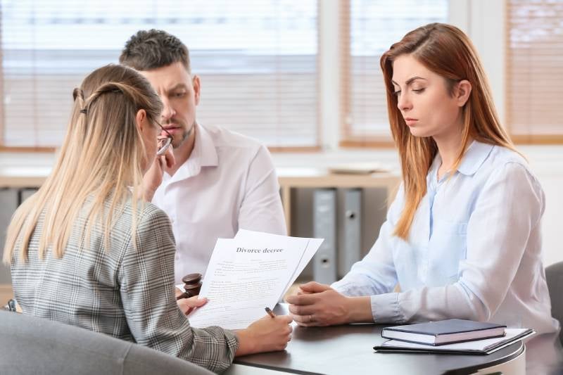 A tense couple sits across from a lawyer reviewing a divorce decree.