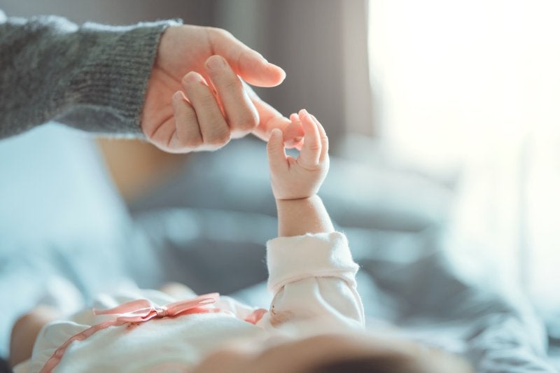 A baby's small hand reaches up to grasp an adult's index finger