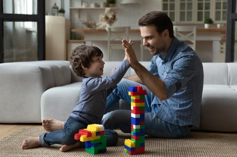 A man and a young boy high-five while playing with colorful blocks