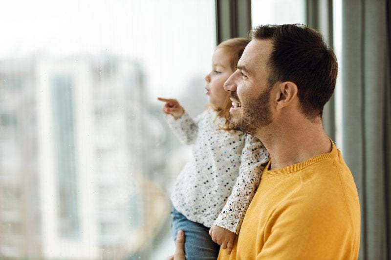 A father and daughter smile while looking out a large window together.