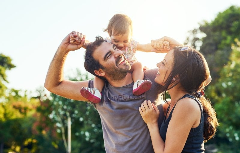 A happy father and mother play with their toddler daughter in a park