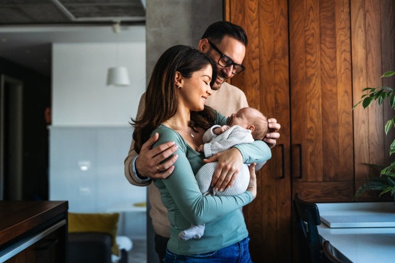A mother and father share a tender moment while holding their sleeping newborn