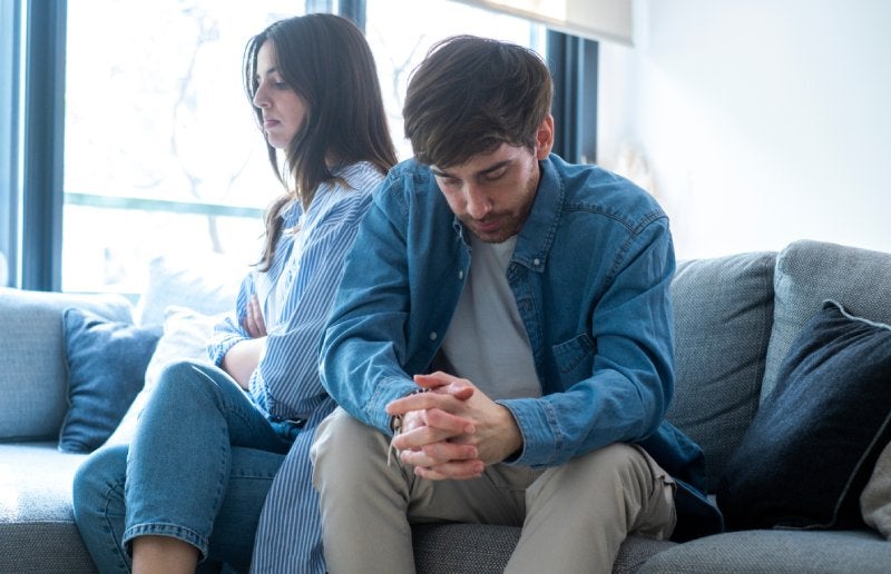 A man sits dejectedly while a woman sits behind him facing away
