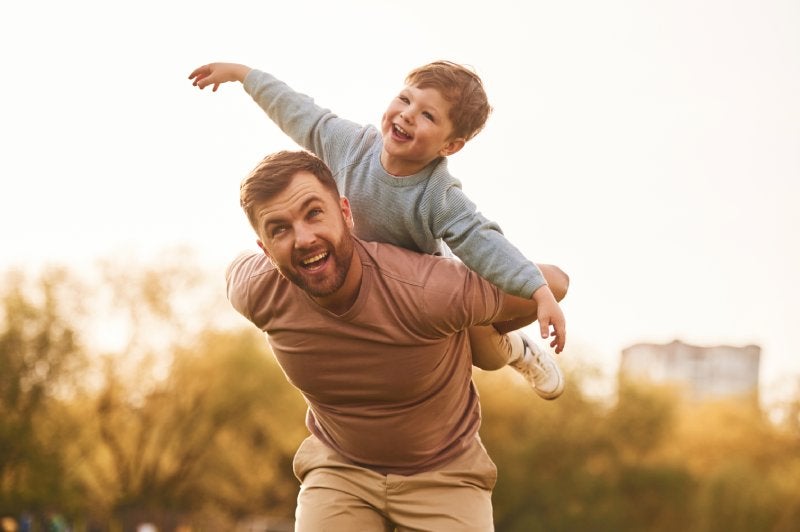 A joyful father gives his young son a piggyback ride outdoors