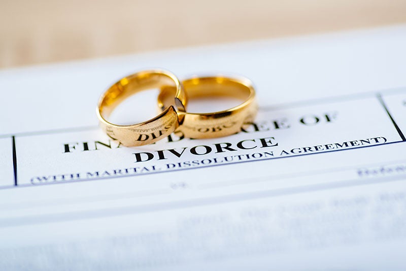 Two gold wedding rings, one broken, resting on a divorce document.