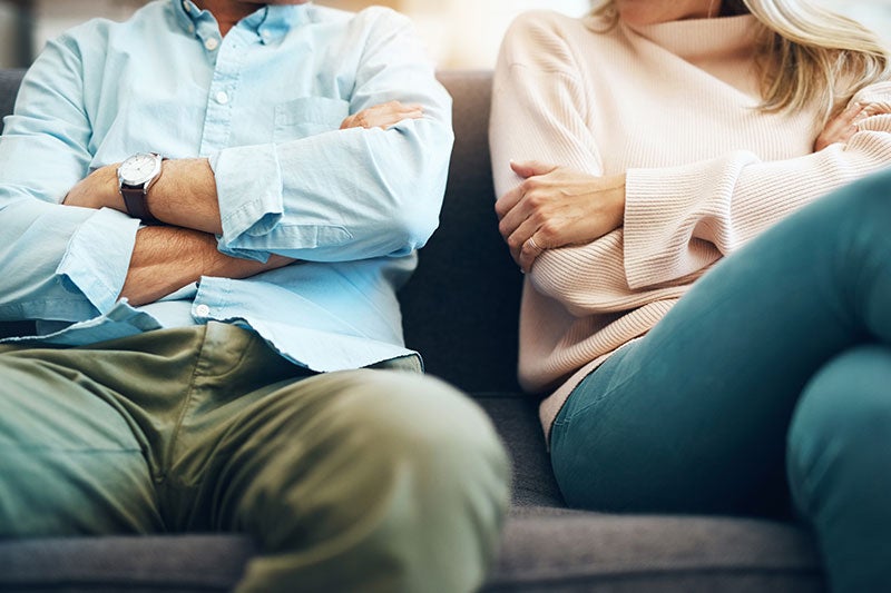 A man and woman sit on a couch with their arms crossed.