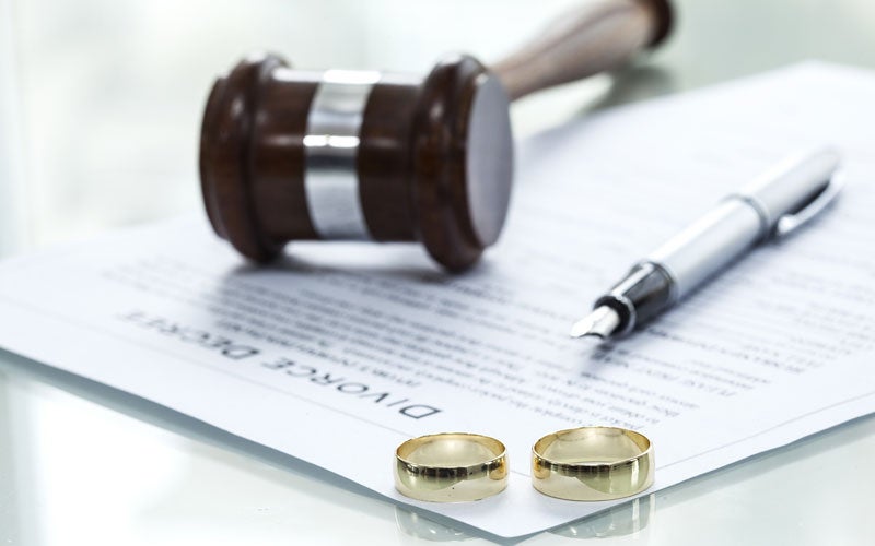 Wedding rings on a divorce decree next to a judge's gavel and pen