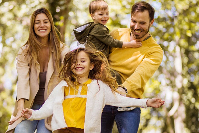 A happy family of four laughs while playing together in the woods