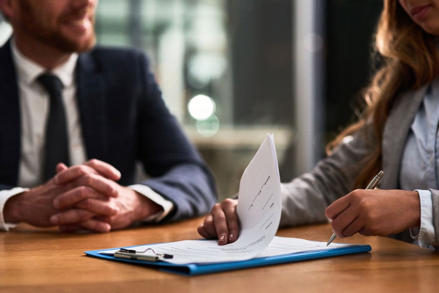 A woman signs a legal document on a clipboard while a man watches