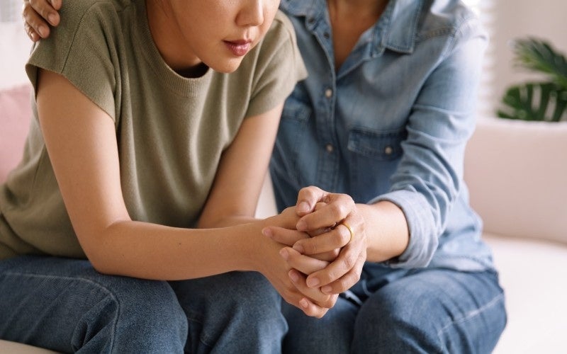 A woman comforts a grieving person by holding their hands and touching their shoulder